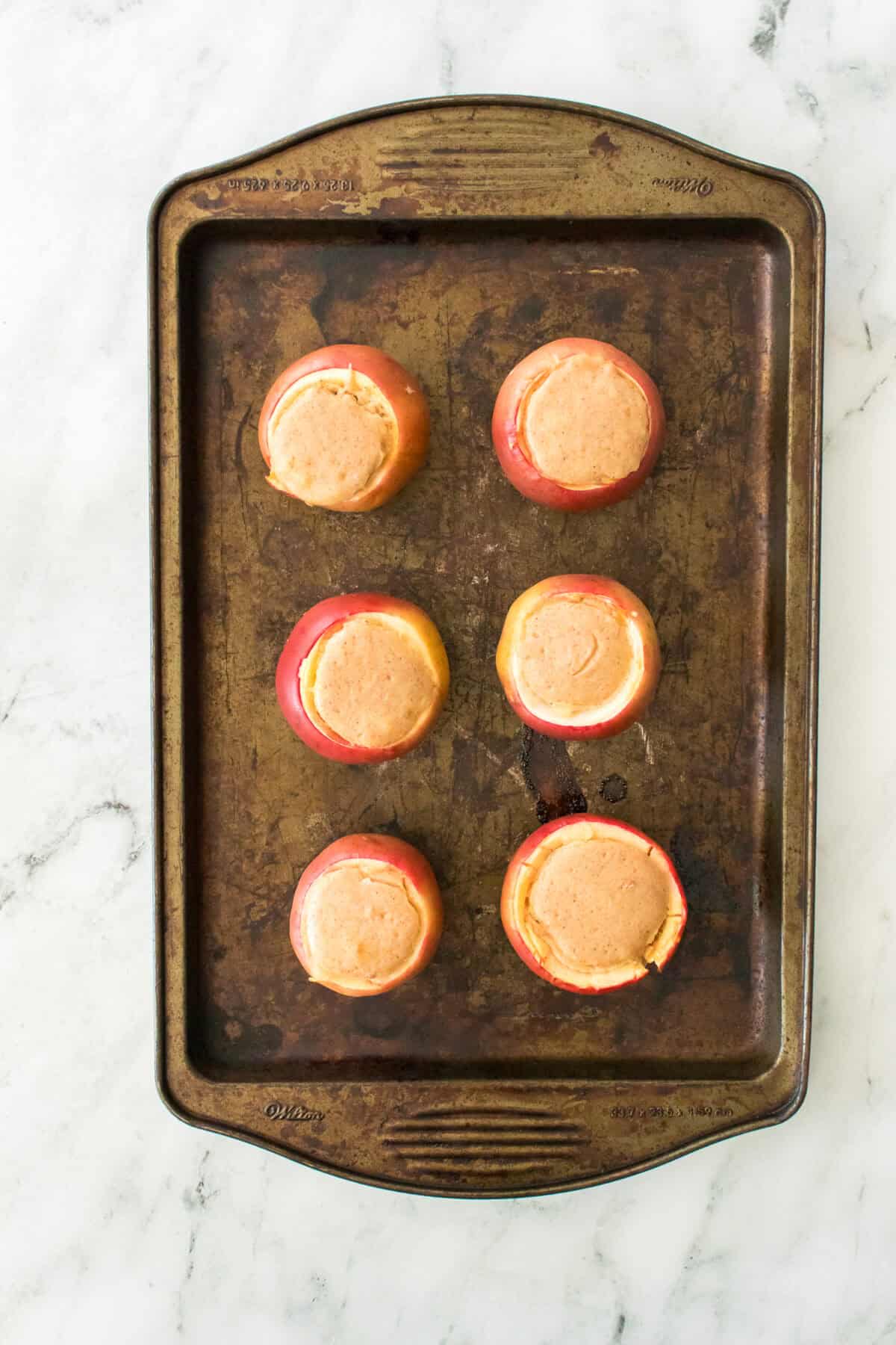 gala apples with stuffed cheesecake filling on baking sheet after being baked