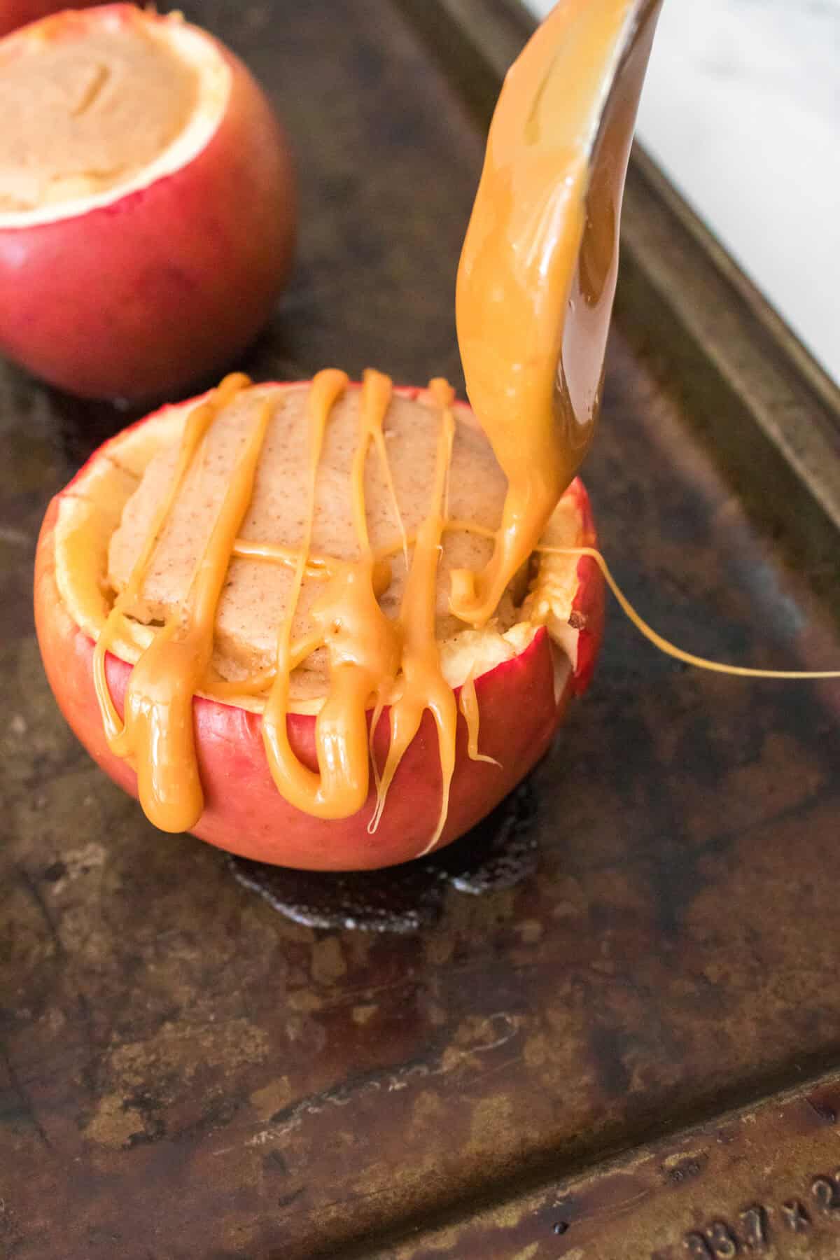 spoon drizzling caramel sauce over baked apple stuffed with cheesecake filling