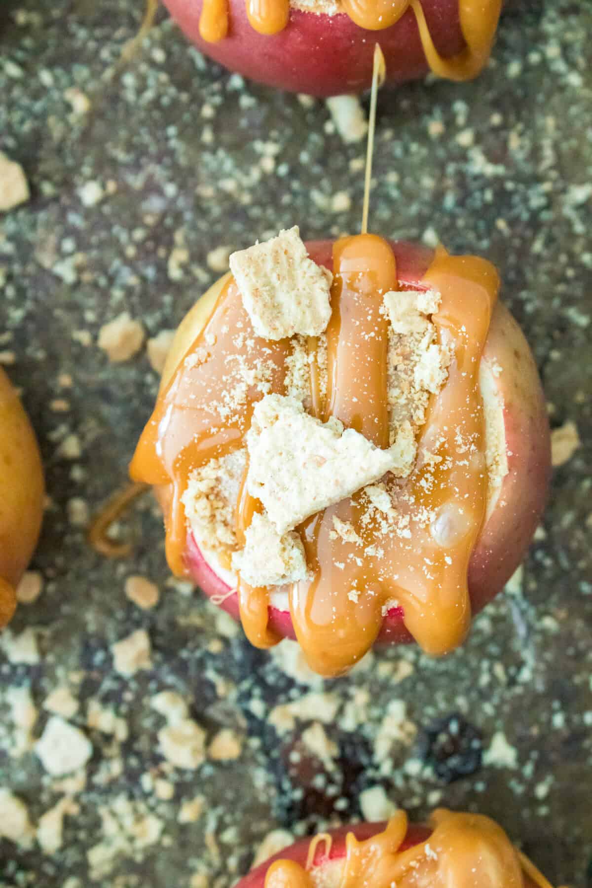 close up overhead shot of cheesecake stuffed apple topped with caramel sauce and graham crackers