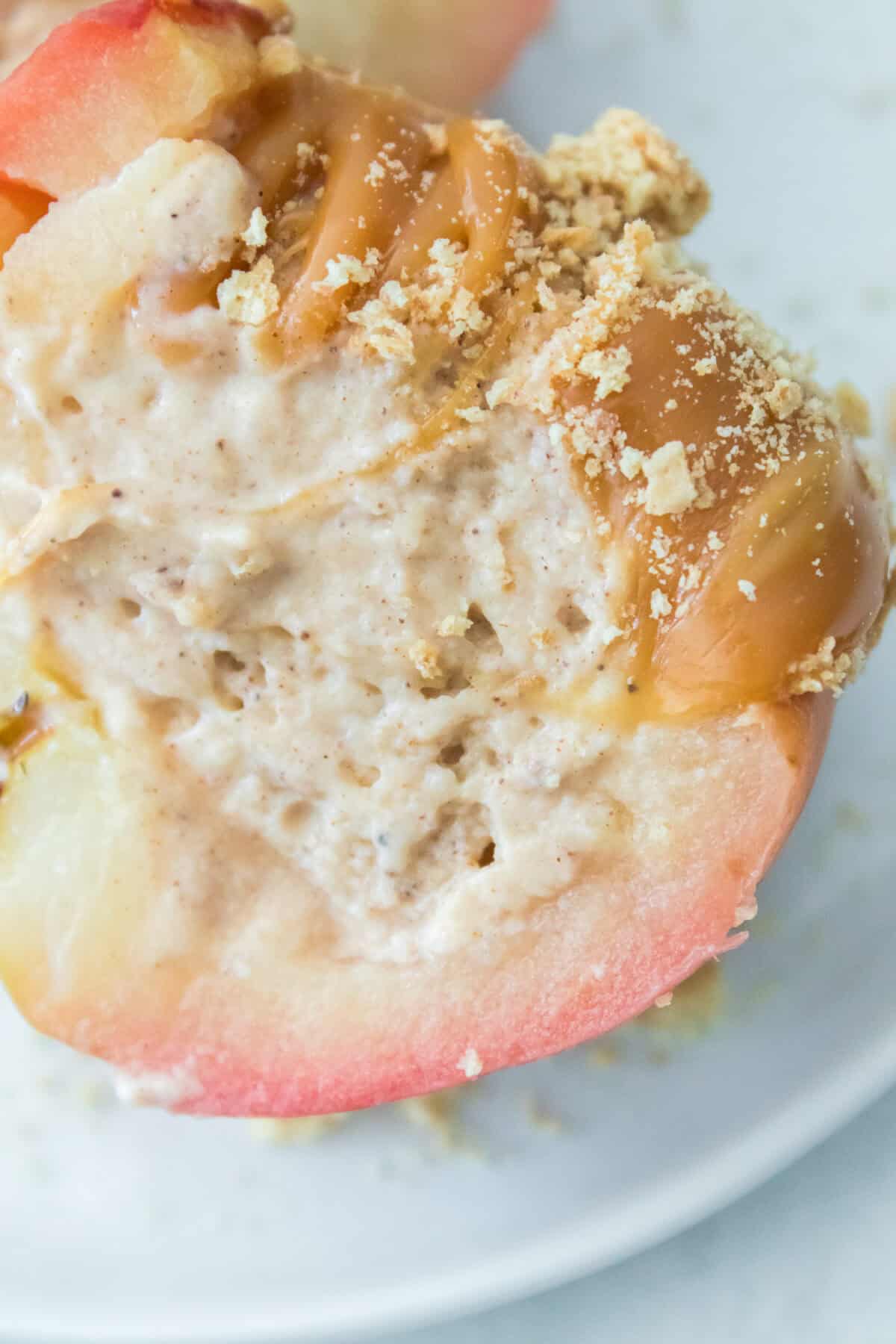 close up vertical shot of cheesecake stuffed apple cut open to see the creamy cheesecake filling inside topped with caramel sauce and graham crackers