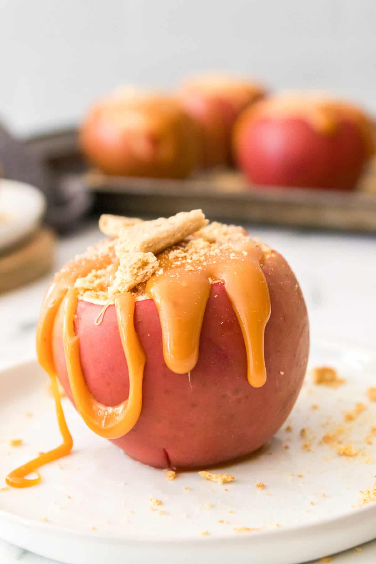 vertical head on shot of baked apple with cheesecake filling, topped with caramel sauce and crushed graham crackers