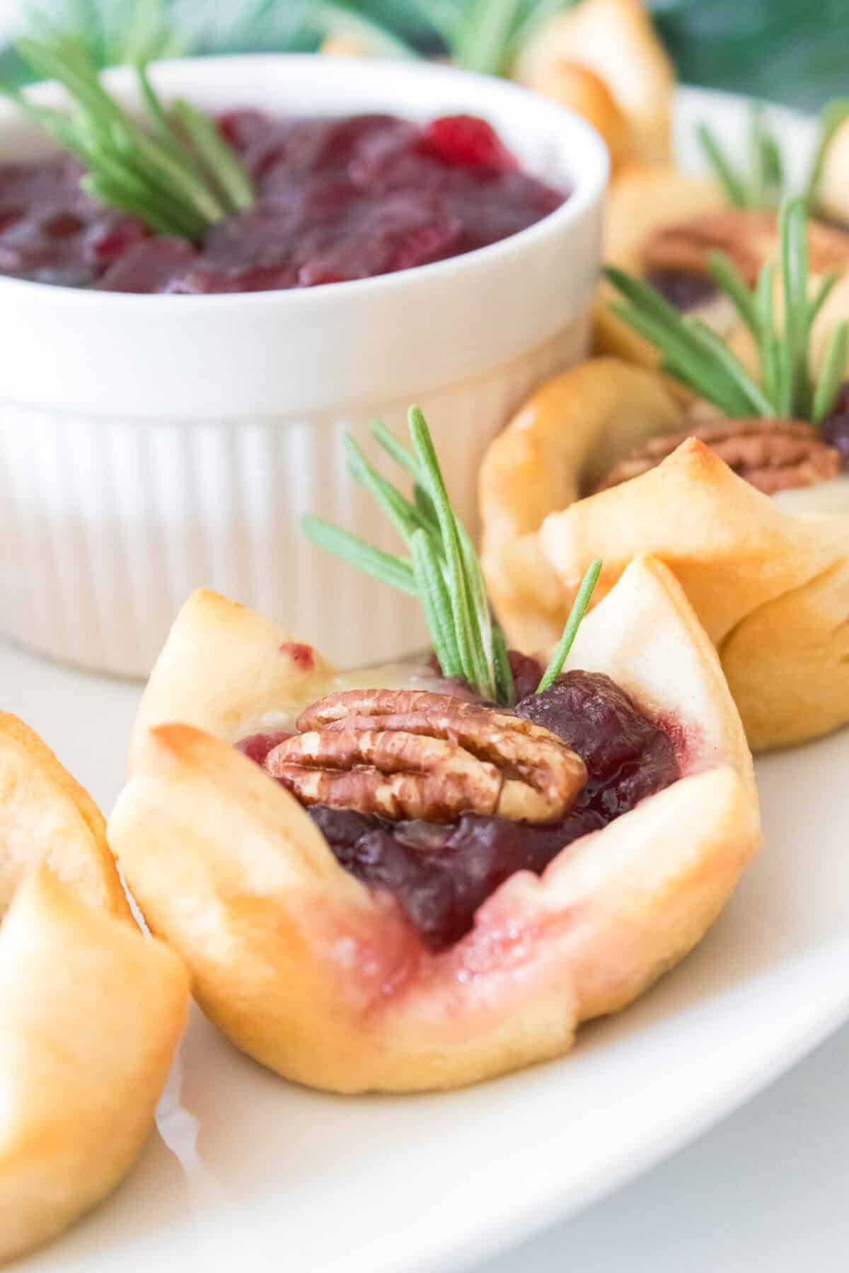 head on vertical shot of cranberry brie bite on serving platter topped with pecan and rosemary