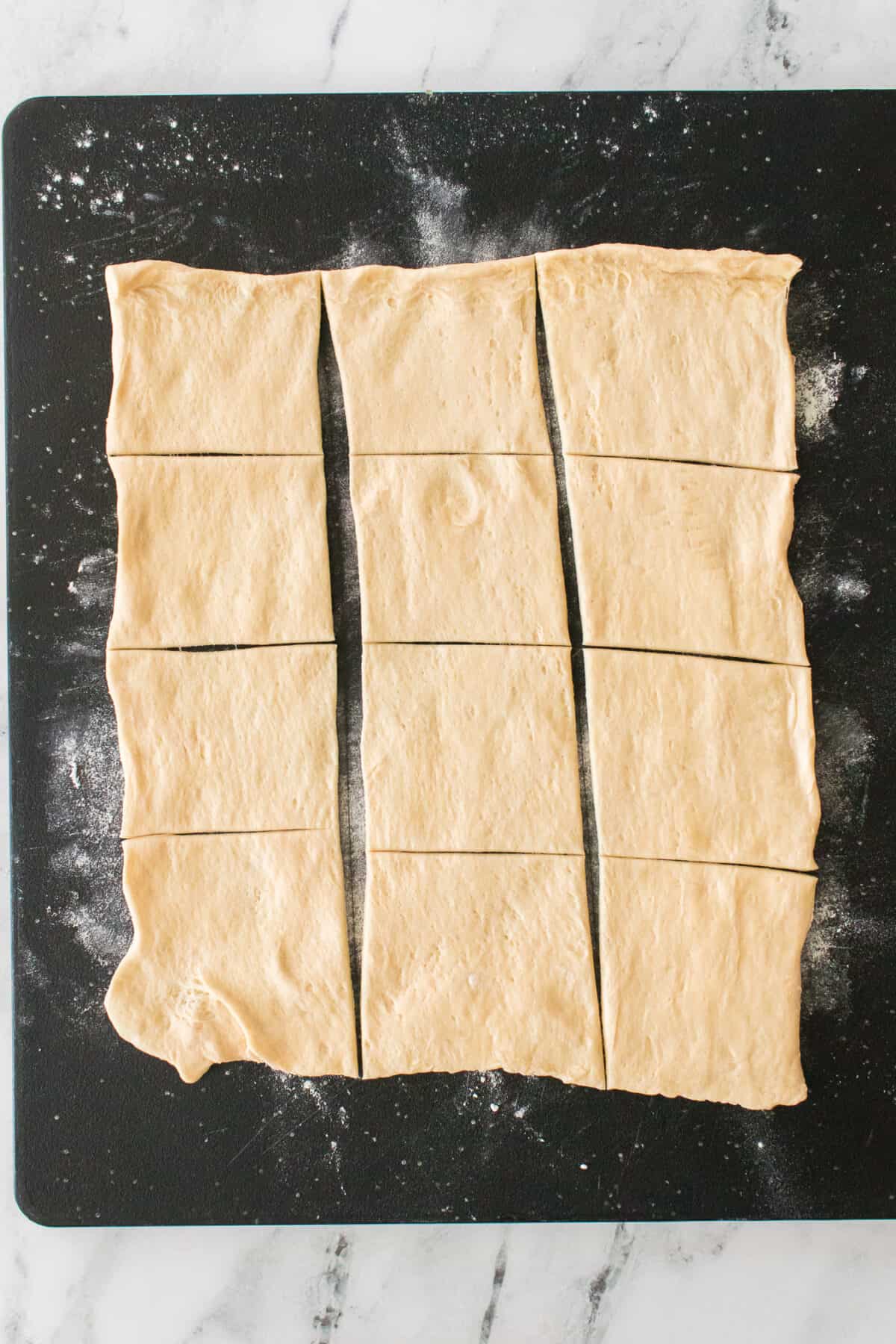 crescent dough on black cutting board dusted with flour cut into 12 pieces