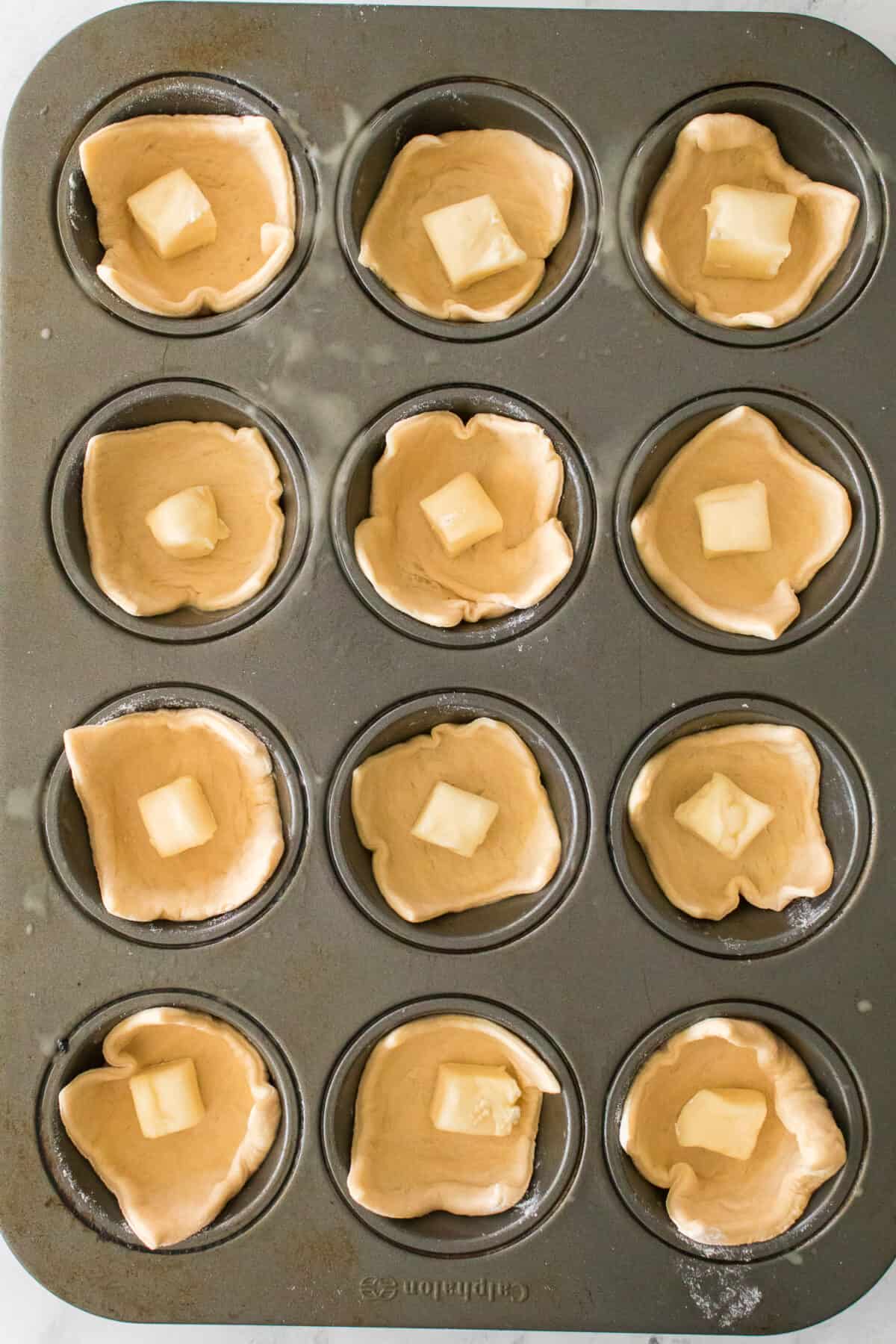 muffin tin with pieces of crescent dough with piece of cubed brie cheese