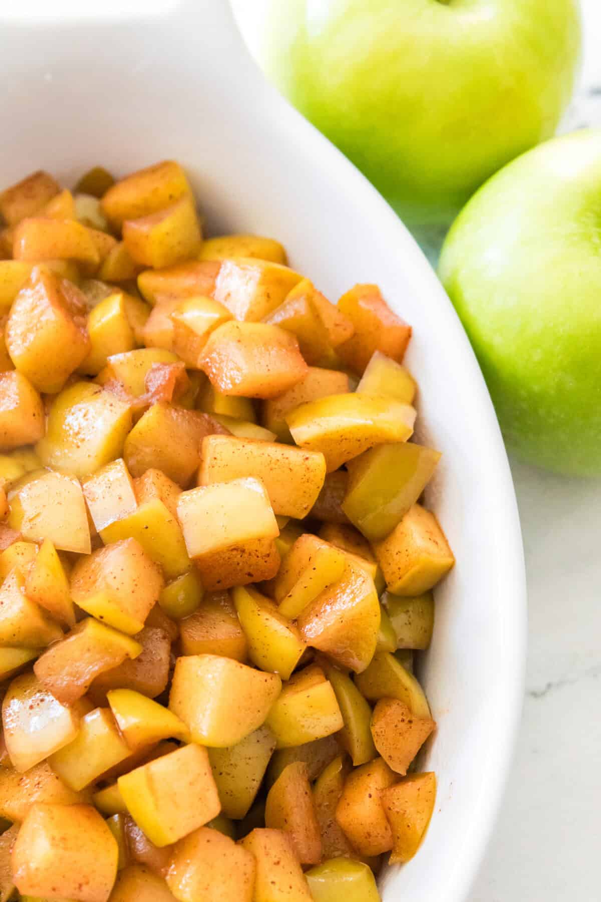 serving dish with warm cinnamon apples with two granny smith apples on the side of the dish