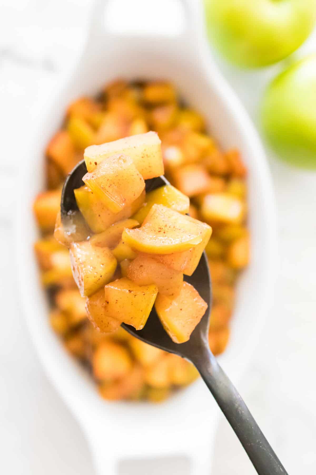 spoonful of cinnamon apples over the top of a serving dish filled with warm cinnamon apples