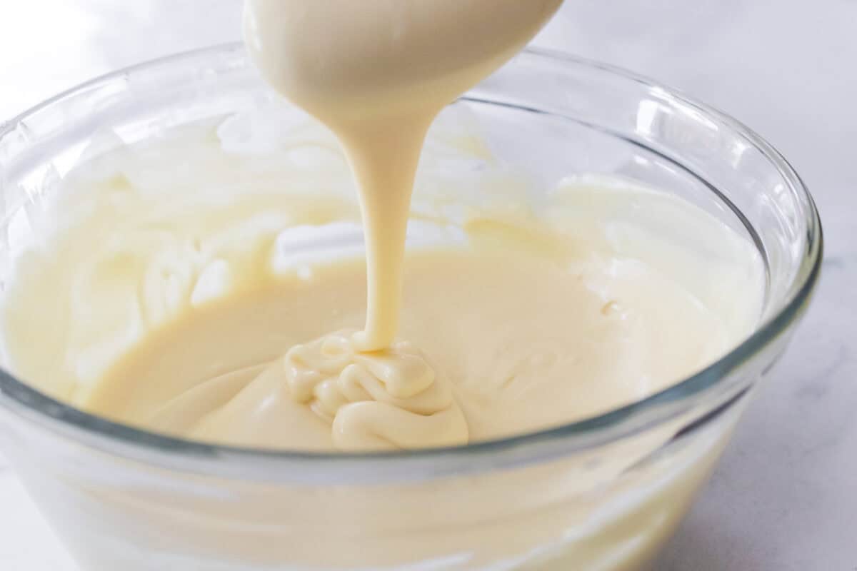 spoon drizzling melted white chocolate with spoon in glass bowl