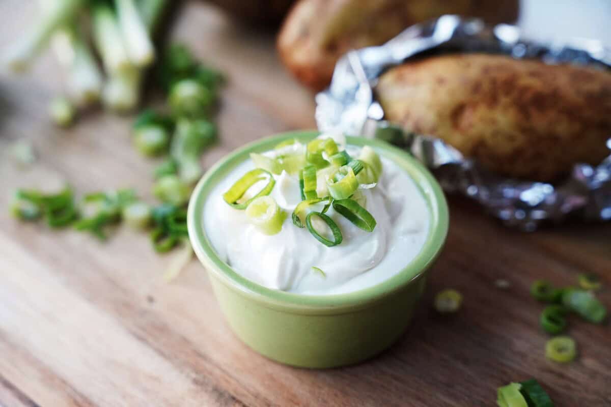 Green onions on top of sour cream with baked potato in the background