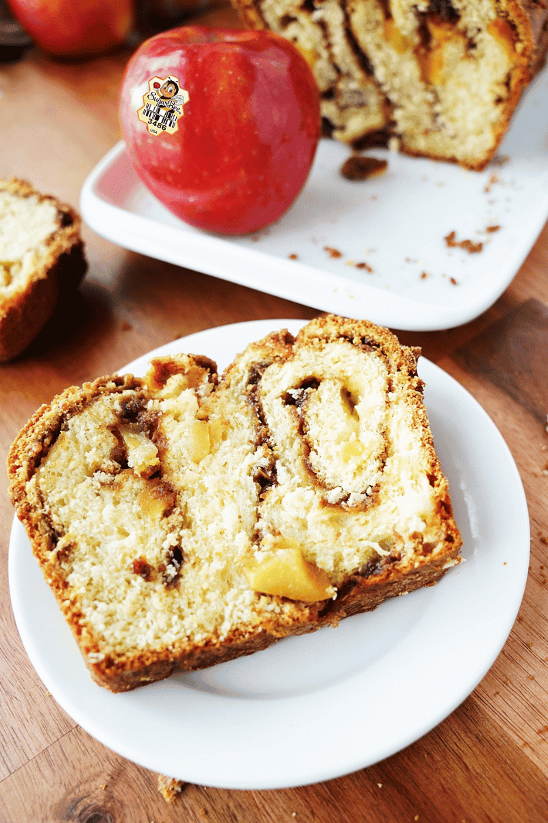 vertical image of a slice of the apple cinnamon babka on a white plate with the loaf behind