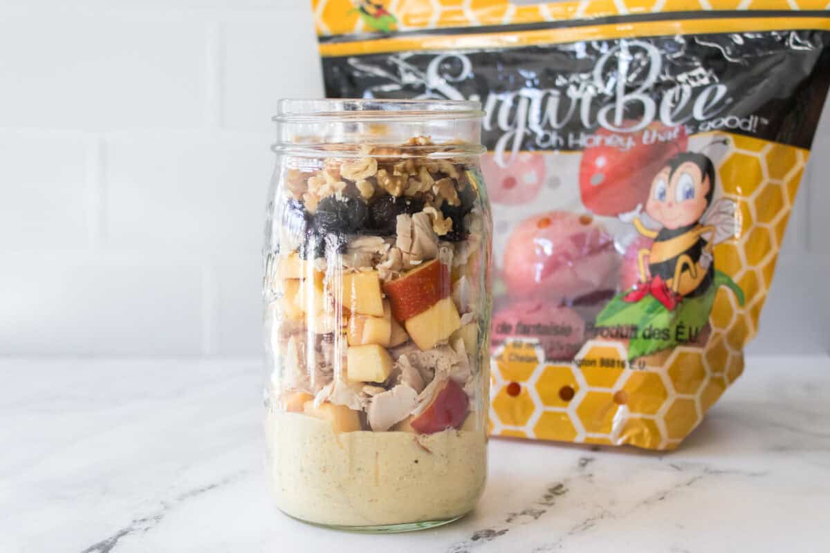 shot of layers of dressing, apples, chicken, dried cranberries and walnuts in mason jar