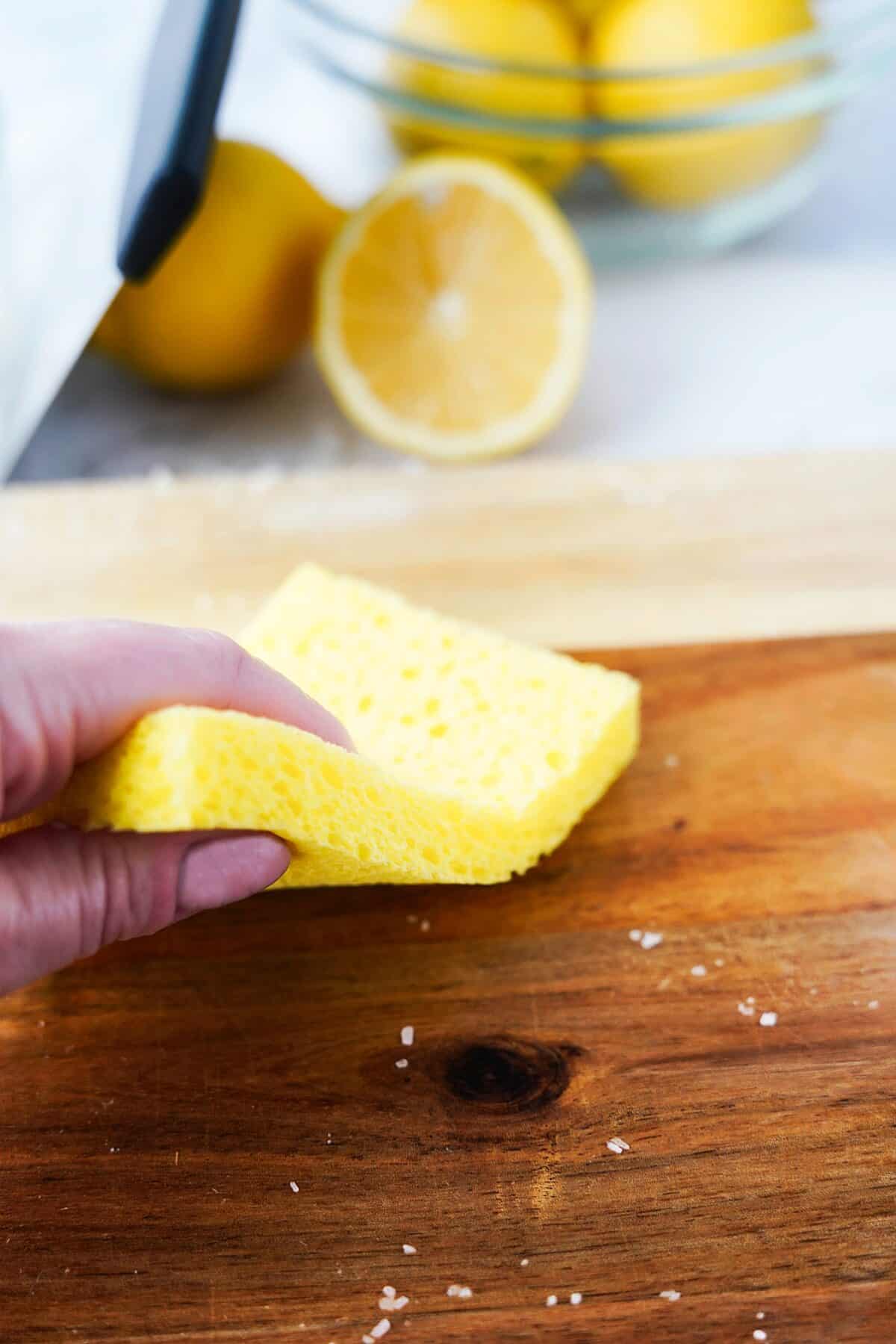 hand using sponge to wipe down wood cutting board