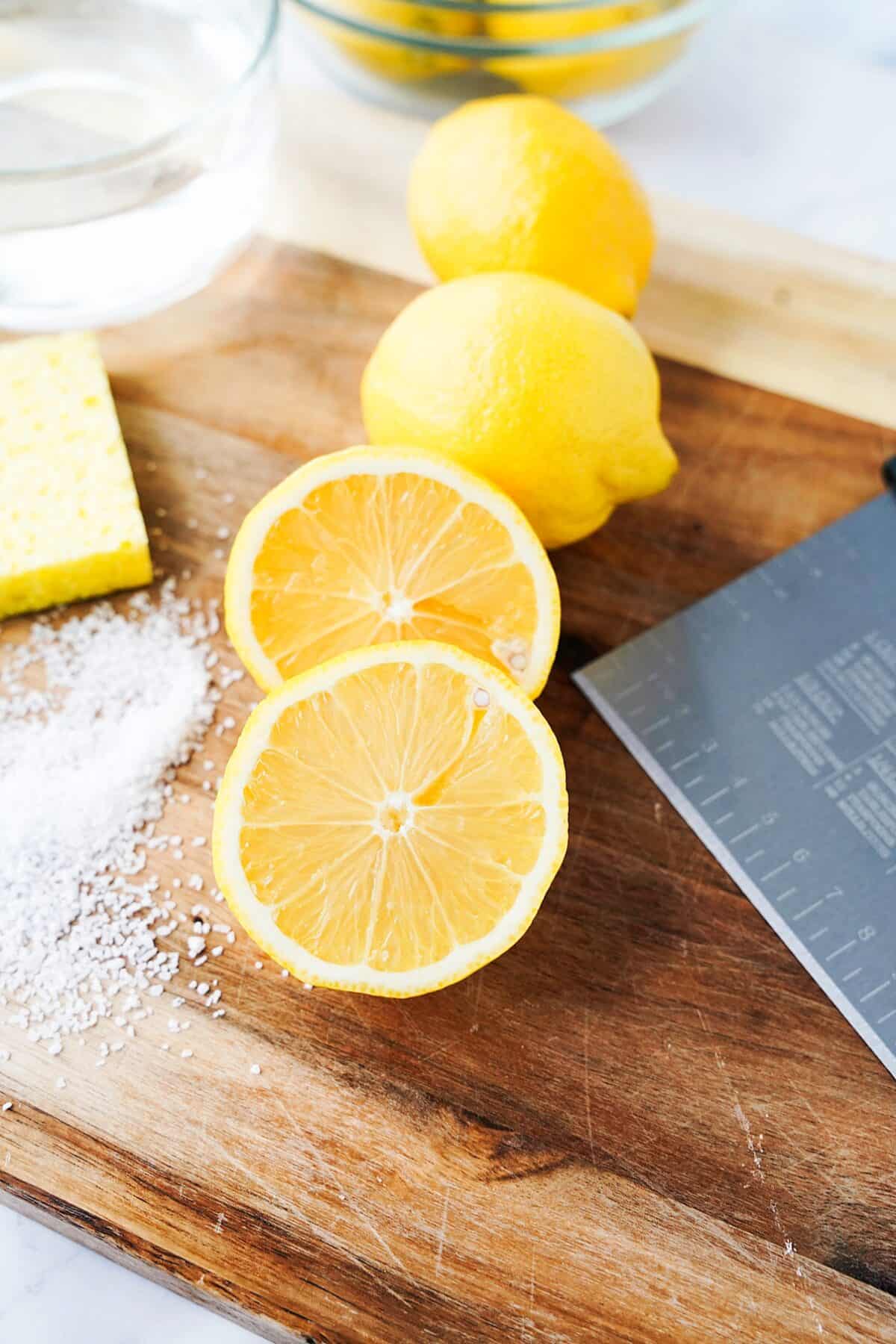 lemon cut in half, sponge, kosher salt and scraper on wood cutting board