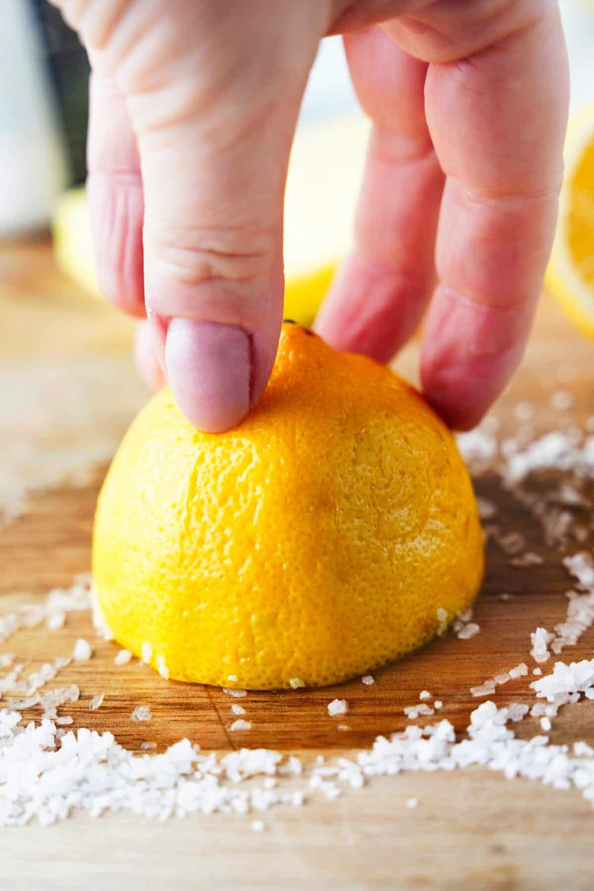 hand using cut lemon with kosher salt to clean wooden cutting board
