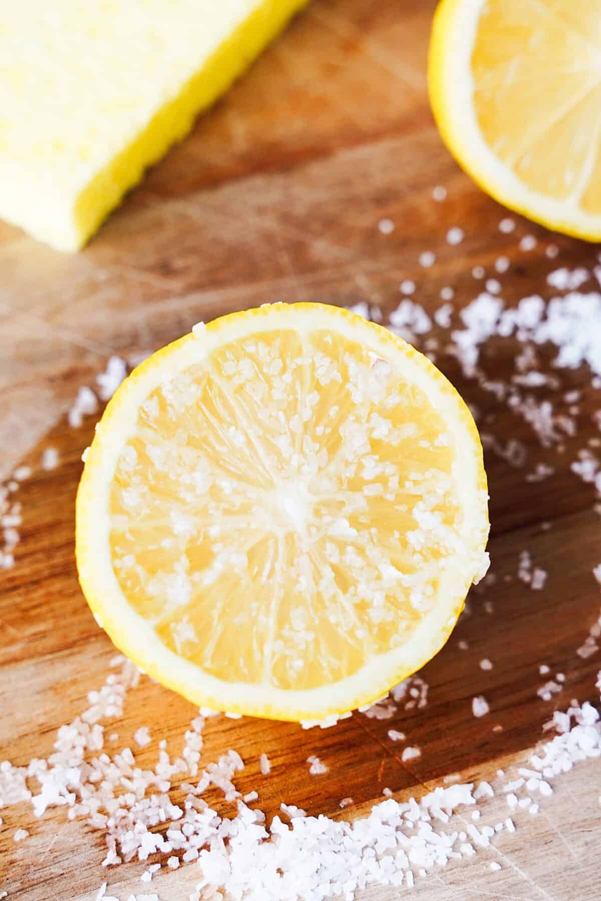 lemon cut in half with kosher salt on it sitting on wood cutting board