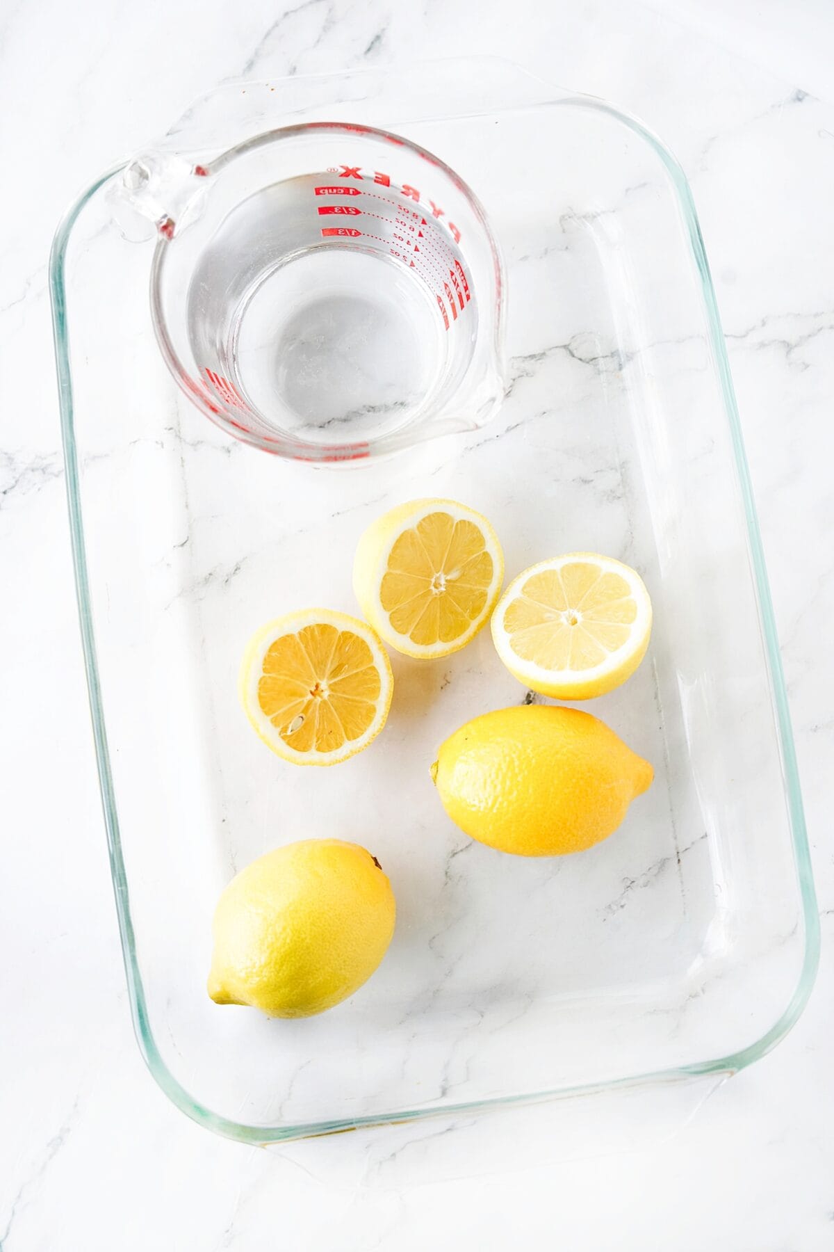 measuring cup of water and lemons in glass baking dish