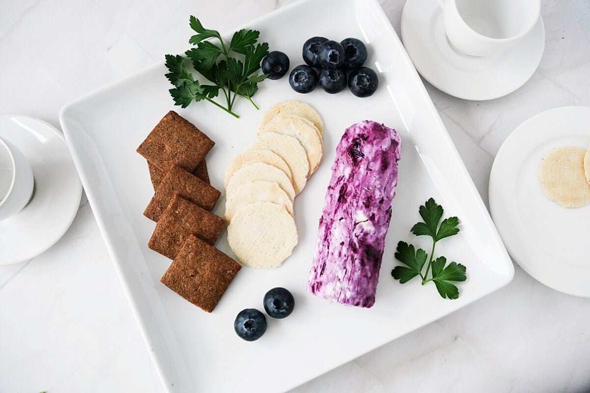 overhead shot of blueberry goat cheese log on white serving platter with crackers and fresh blueberries