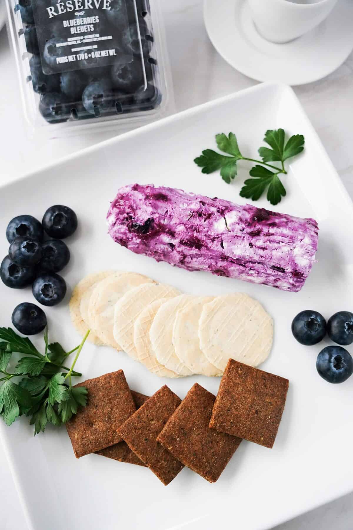 vertical shot of blueberry goat cheese log on plate with crackers, fresh blueberries and parsley