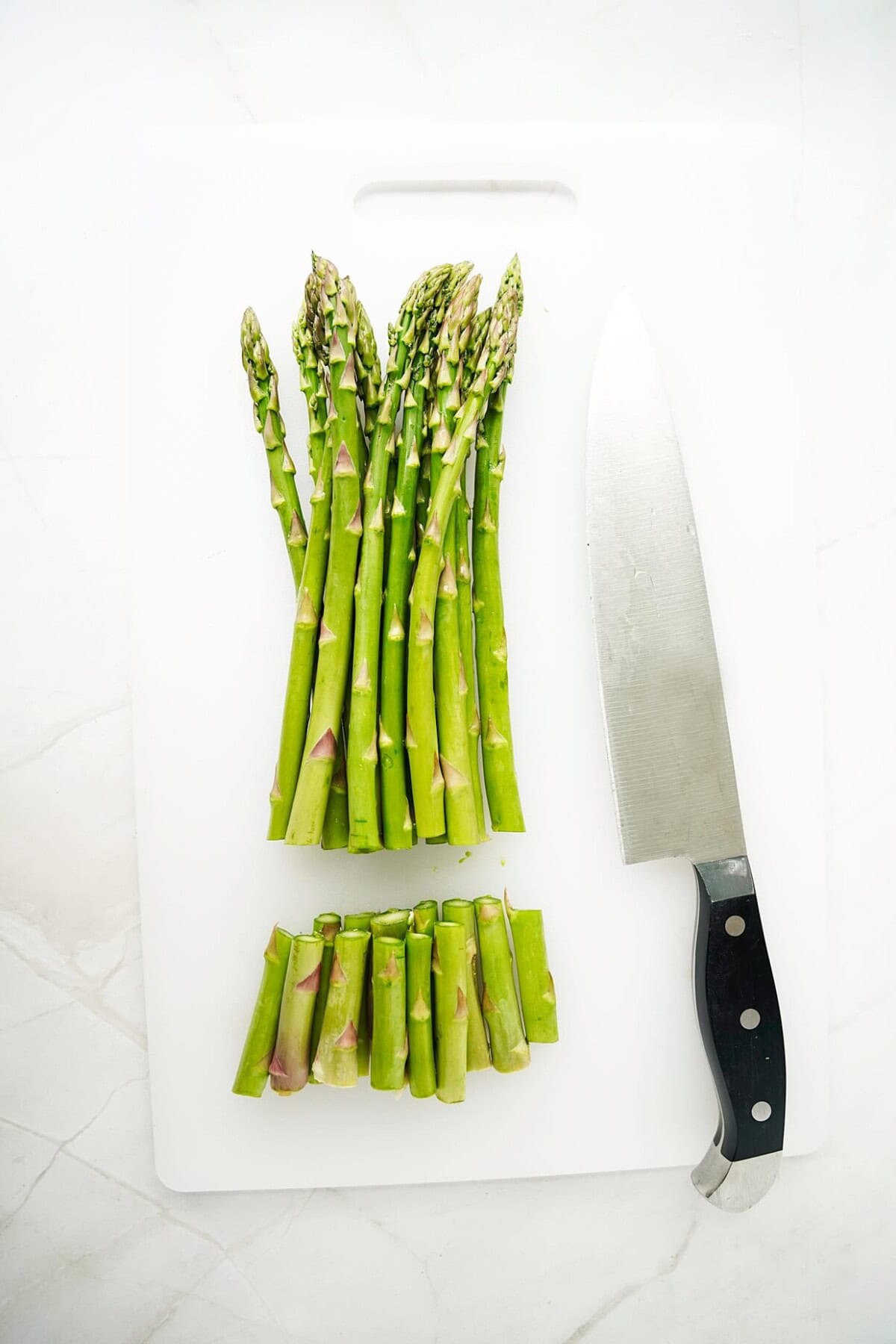 Cut asparagus on white cutting board with knife