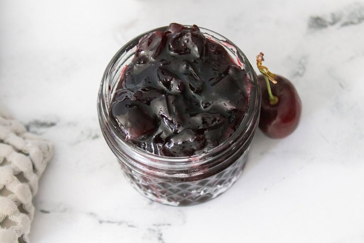 overhead 45 degree shot of cherry preserves in jelly jar with cherry on side
