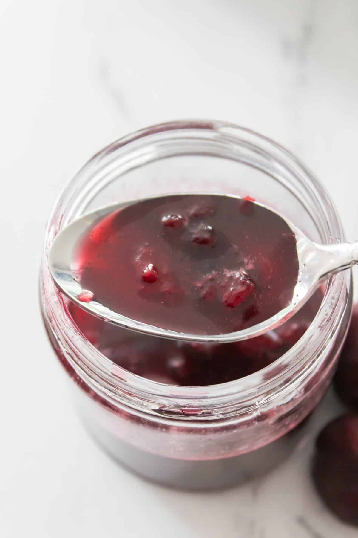 vertical shot of spoon of cherry vanilla syrup over mason jar
