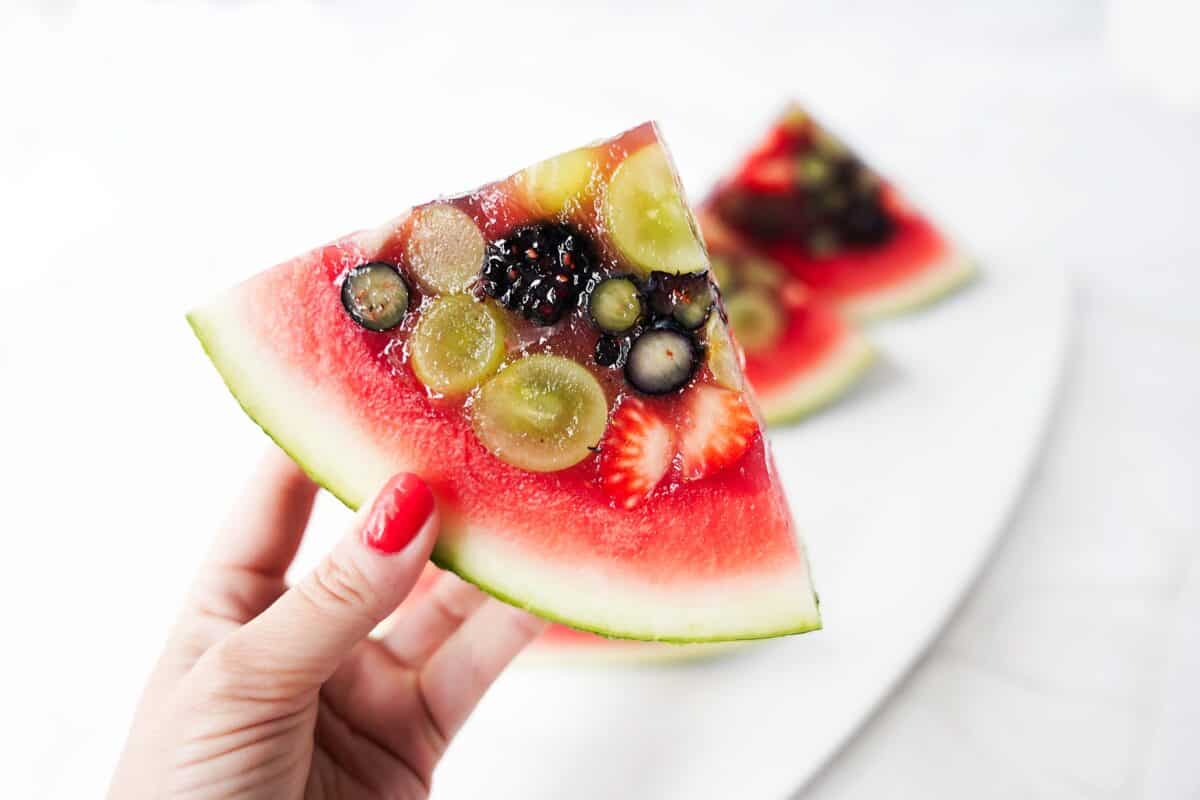 hand holding watermelon slices with jello stuffed with fresh fruit