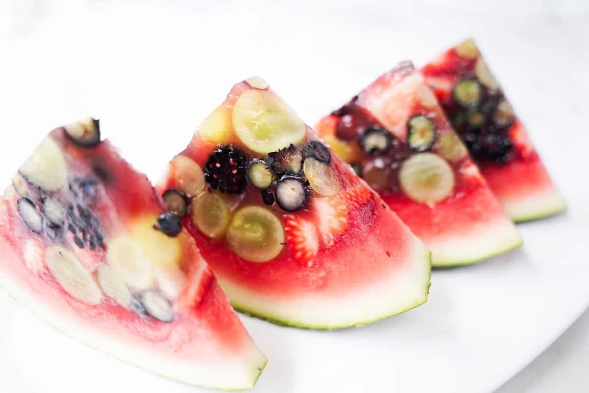 slices of watermelon that has been poured with jello and fresh fruit on white serving platter