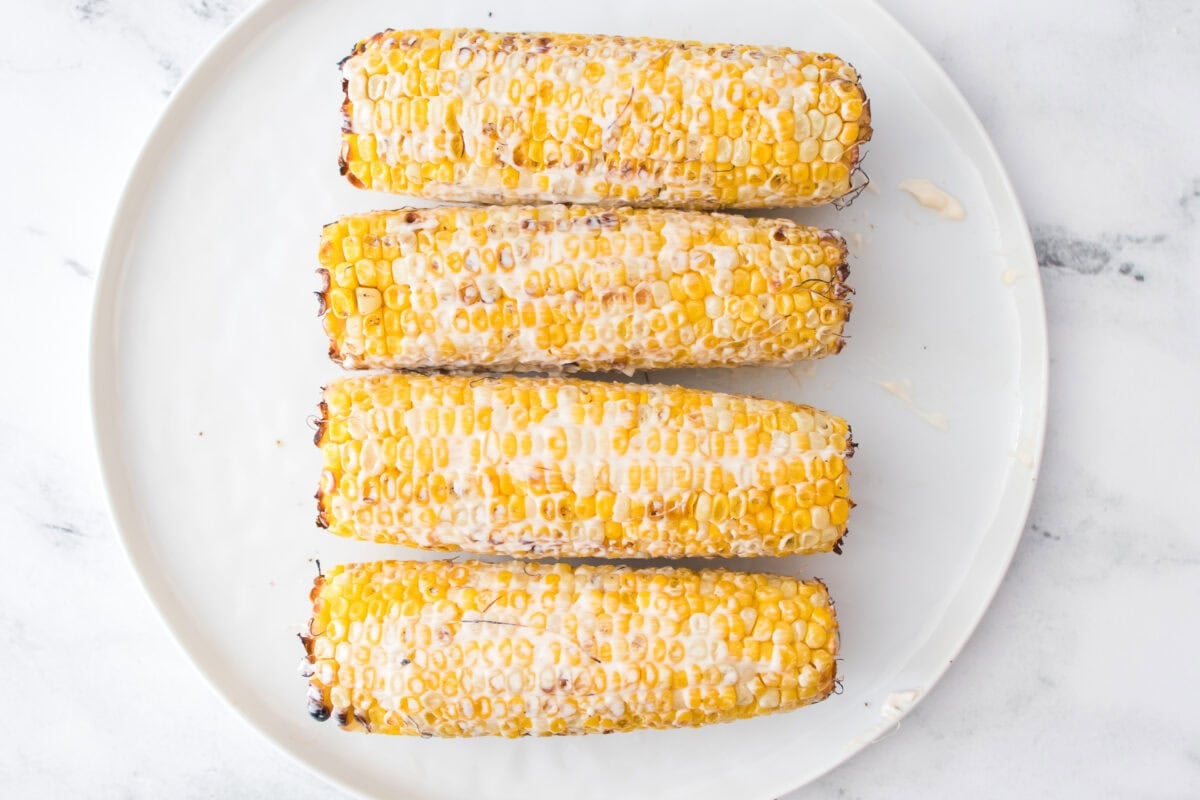 grilled corn slathered in mayo on white plate