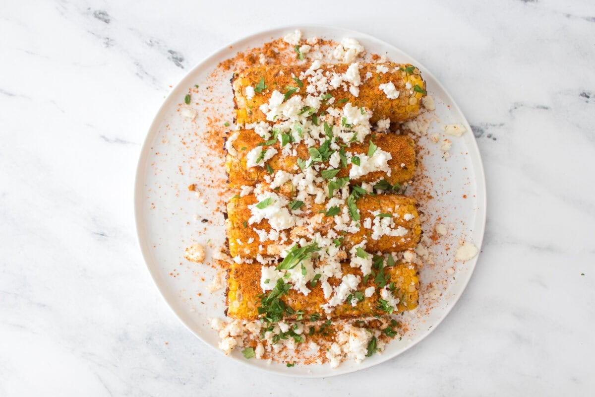 grilled corn that's been coated with mayo, lime juice, elote seasoning, cojita cheese and cilantro on white plate