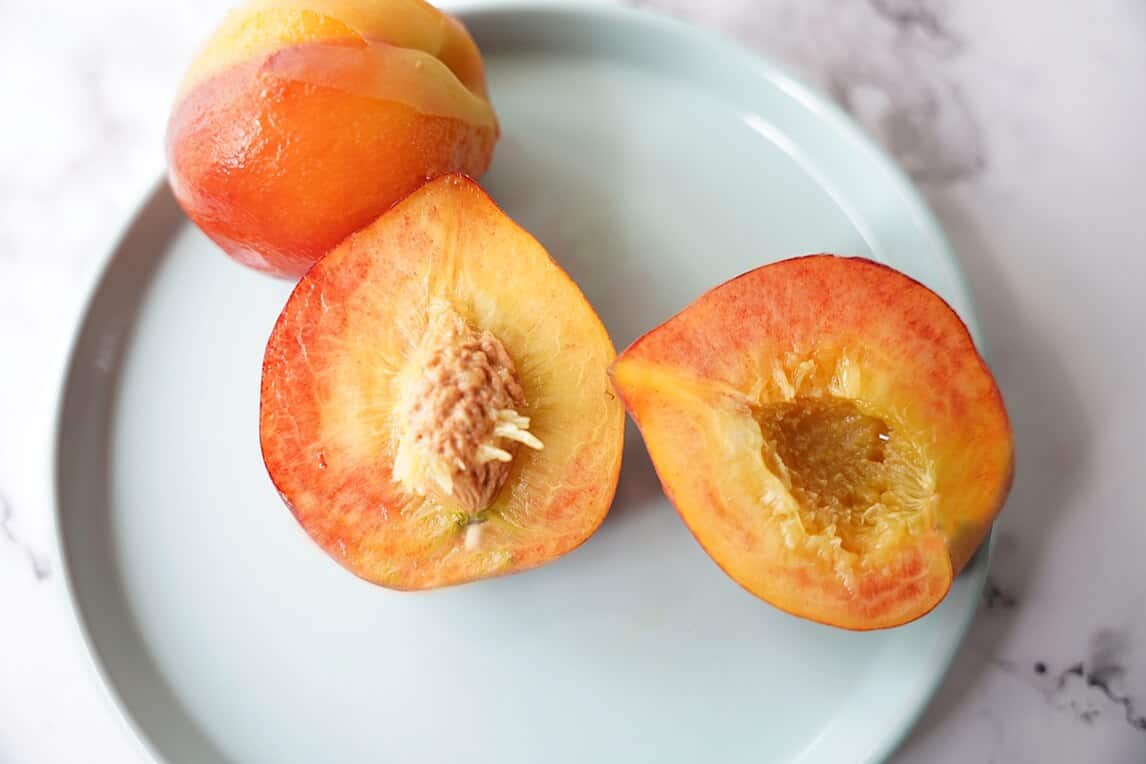 Halved peeled peaches on a plate with the pit exposed