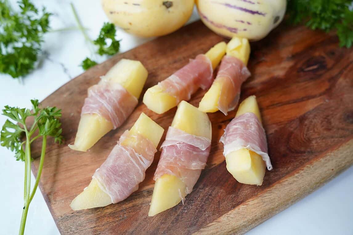 Prosciutto wrapped pepino melon on cutting board