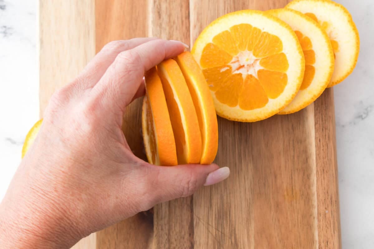 hand holding slices of oranges on cutting board to show thickness of oranges