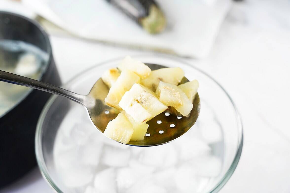 Pieces of eggplant on slotted spoon getting blanced