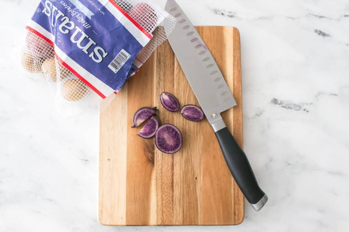 overhead shot of knife on cutting board with a smalls medley potato that has been quartered