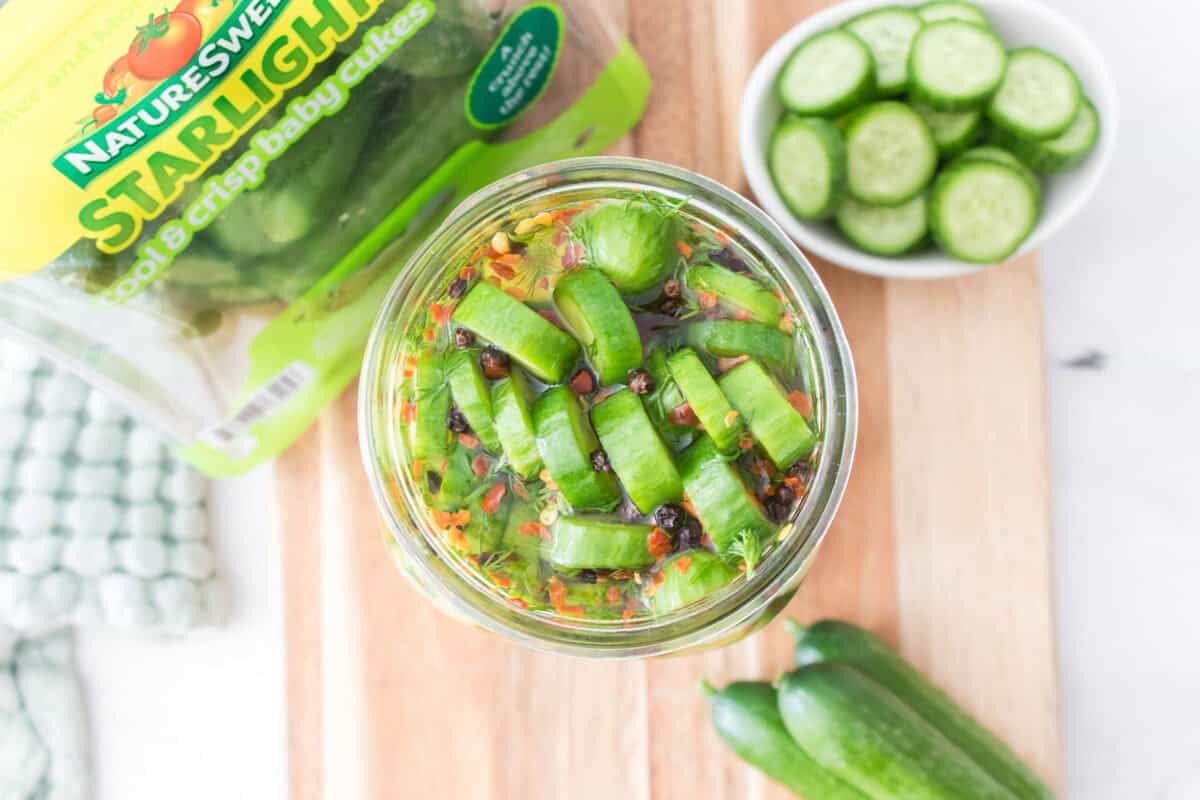 overhead shot of mason jar with quick pickled cucumbers with naturesweet starlight baby cukes packaging, bowl of sliced baby cukes on cutting board
