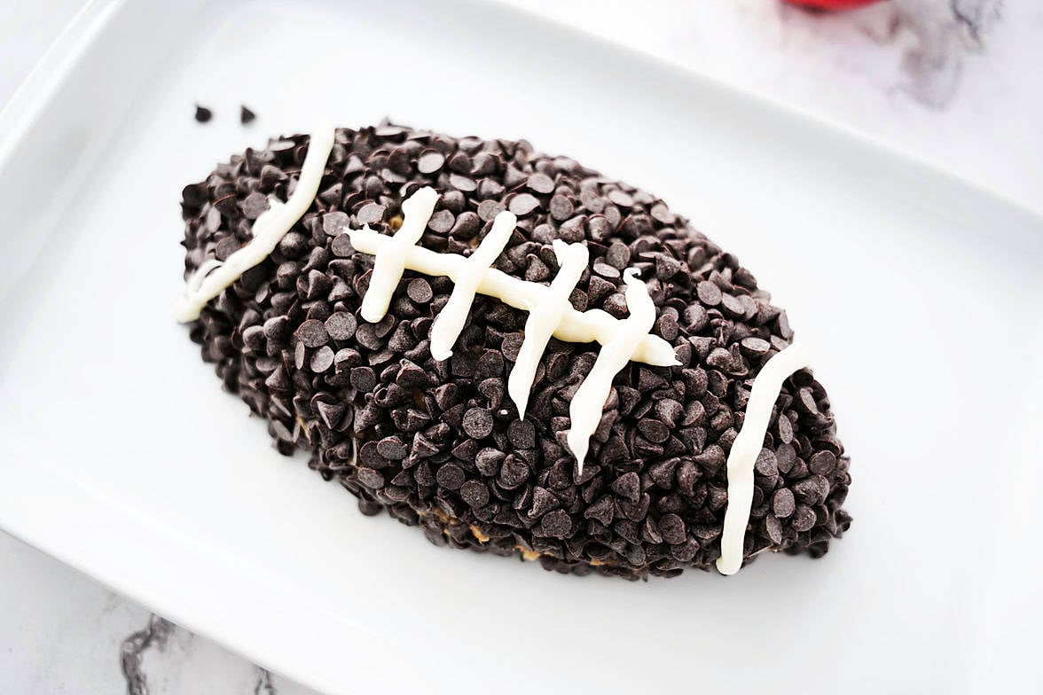 white serving platter with apple toffee dip after being shaped into a football, topped with mini morsels and white icing for laces of the football