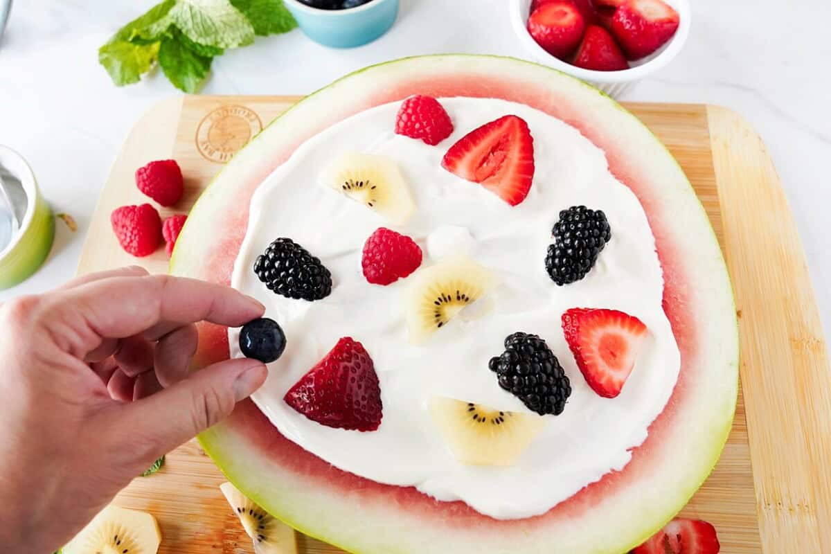 fruit being placed on cream cheese dip on top of watermelon