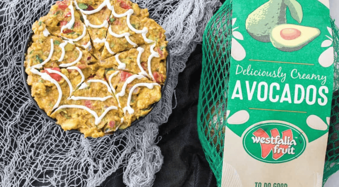 Spiderweb Guacamole in bowl with a bag of Westfalia Fruit avocados to the right