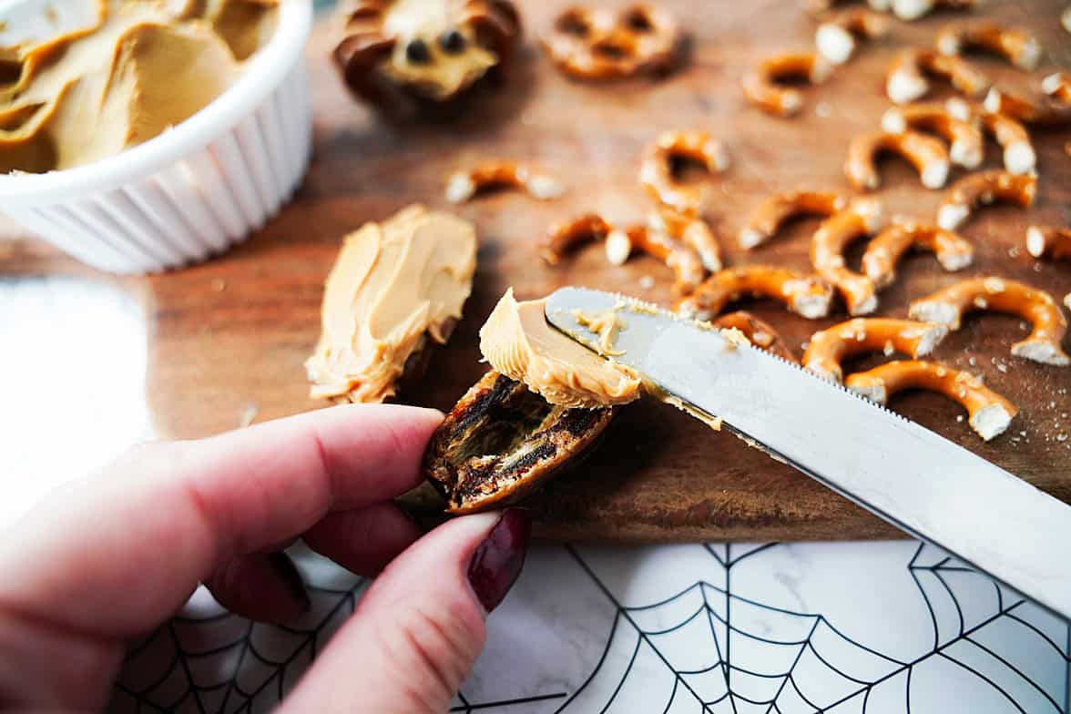hand holding date that has been slider in half, spreading peanut butter over the top with a butter knife