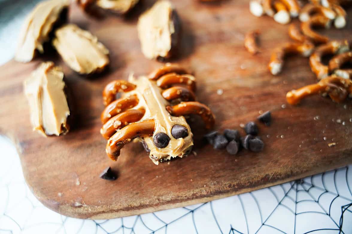 spider made out of a date sliced in half, peanut butter, broken pretzel pieces for leg and mini chocolate chips for eyes on cutting board