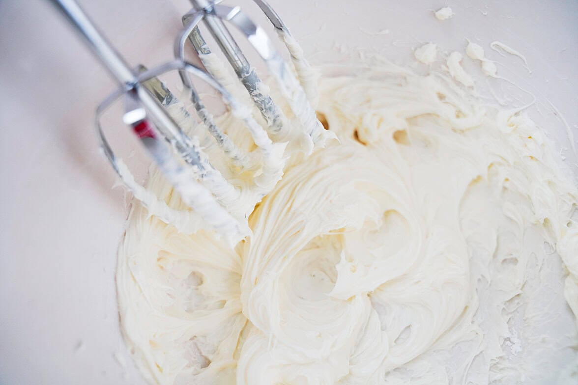 cream cheese and powdered sugar being beat together in a white bowl with a hand mixer