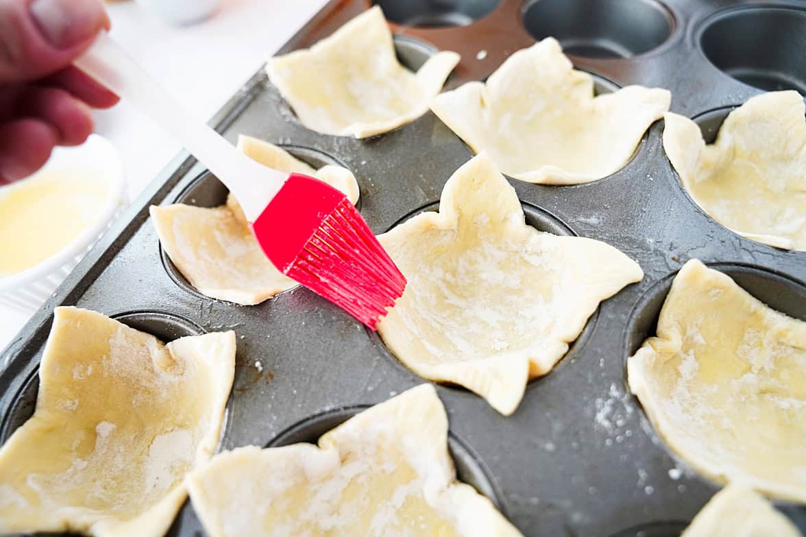 brush putting on egg wash on puff pastry in muffin tin