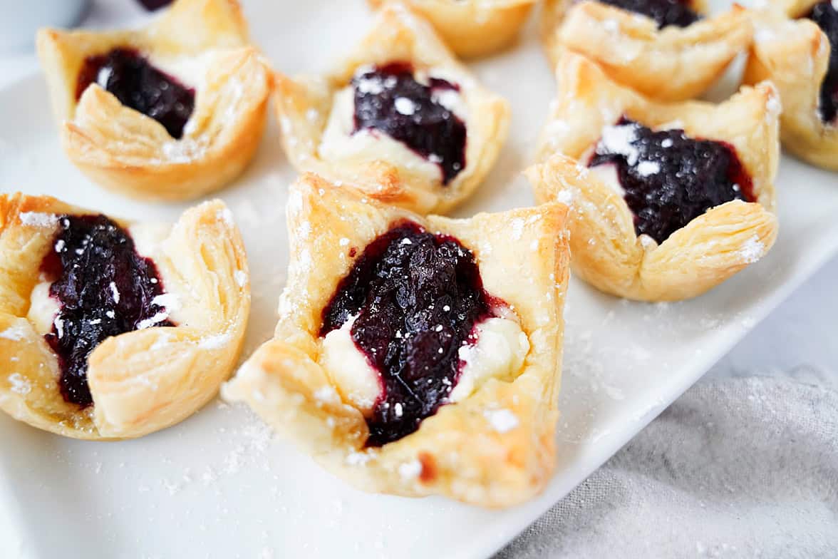 sugar plum danishes on white serving platter dusted with powdered sugar