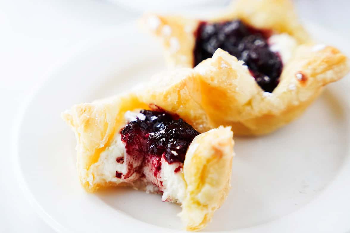two sugar plum danishes on white plate with bite taken out of one