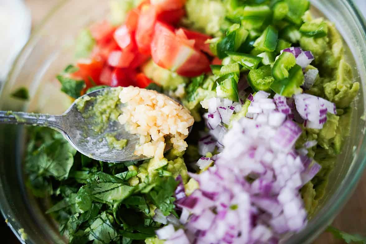 overhead shot of all ingredients to make homemade guacamole in glass bowl before mixing: