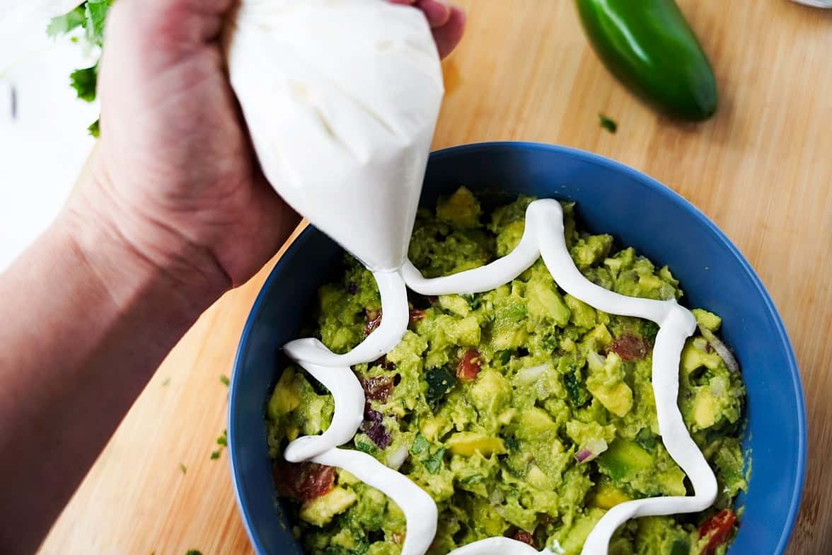 Using the sour cream in a plastic bag to make a concentric circle on top of the guacamole in a bowl