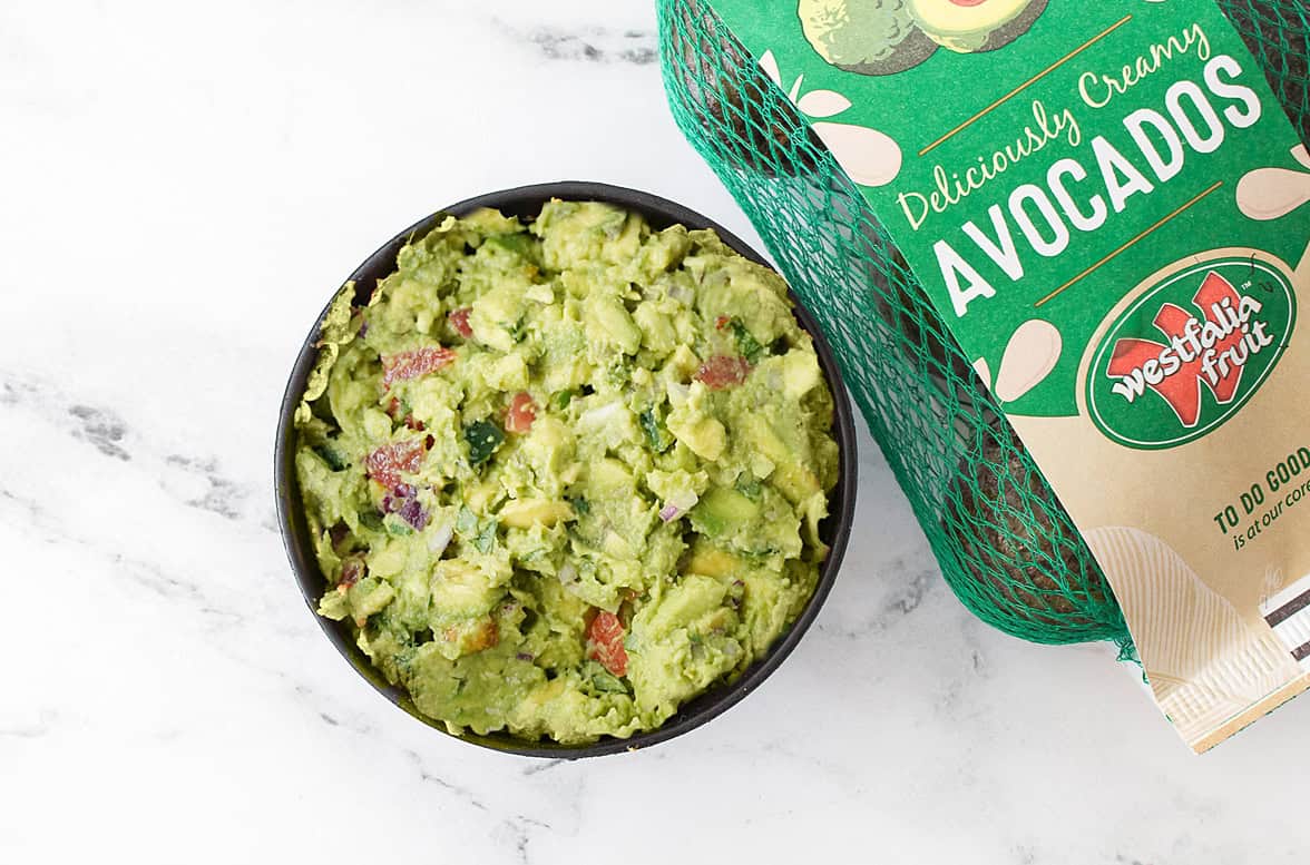 overhead shot of guacamole in guacamole bowl with bag of Westfalia Fruit avocados
