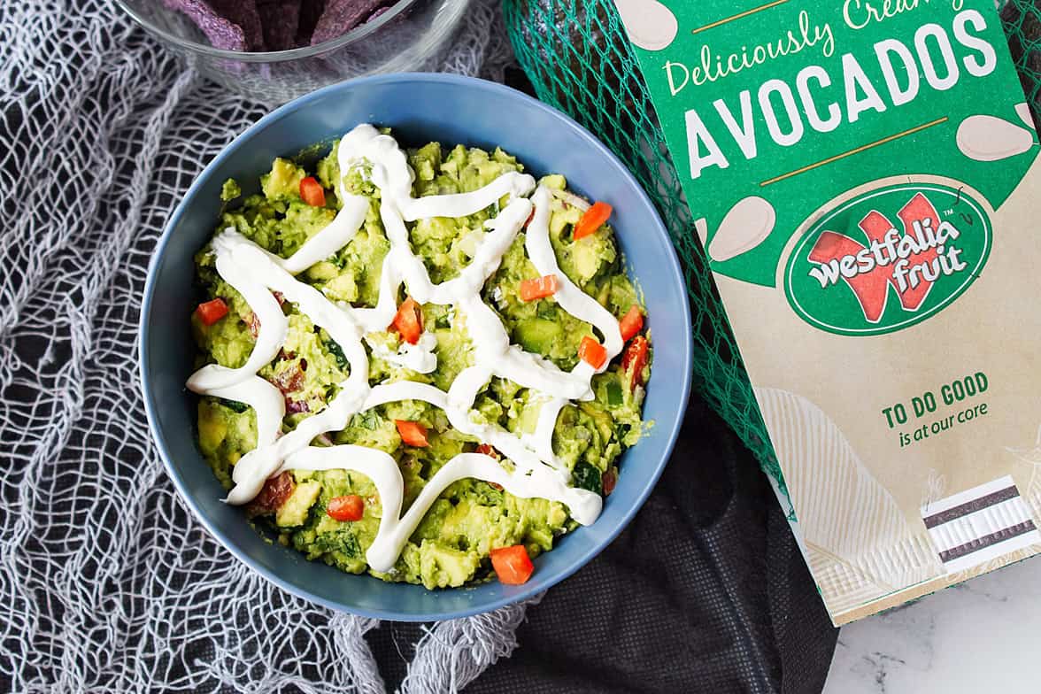 overhead shot of spiderweb guacamole with bag of Westfalia Fruit avocados with a