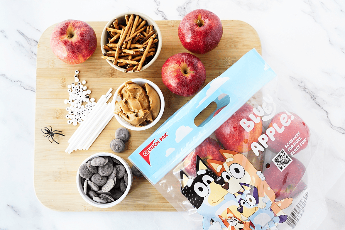 Apples, peanut butter, pretzels, and chocolate on a cutting board