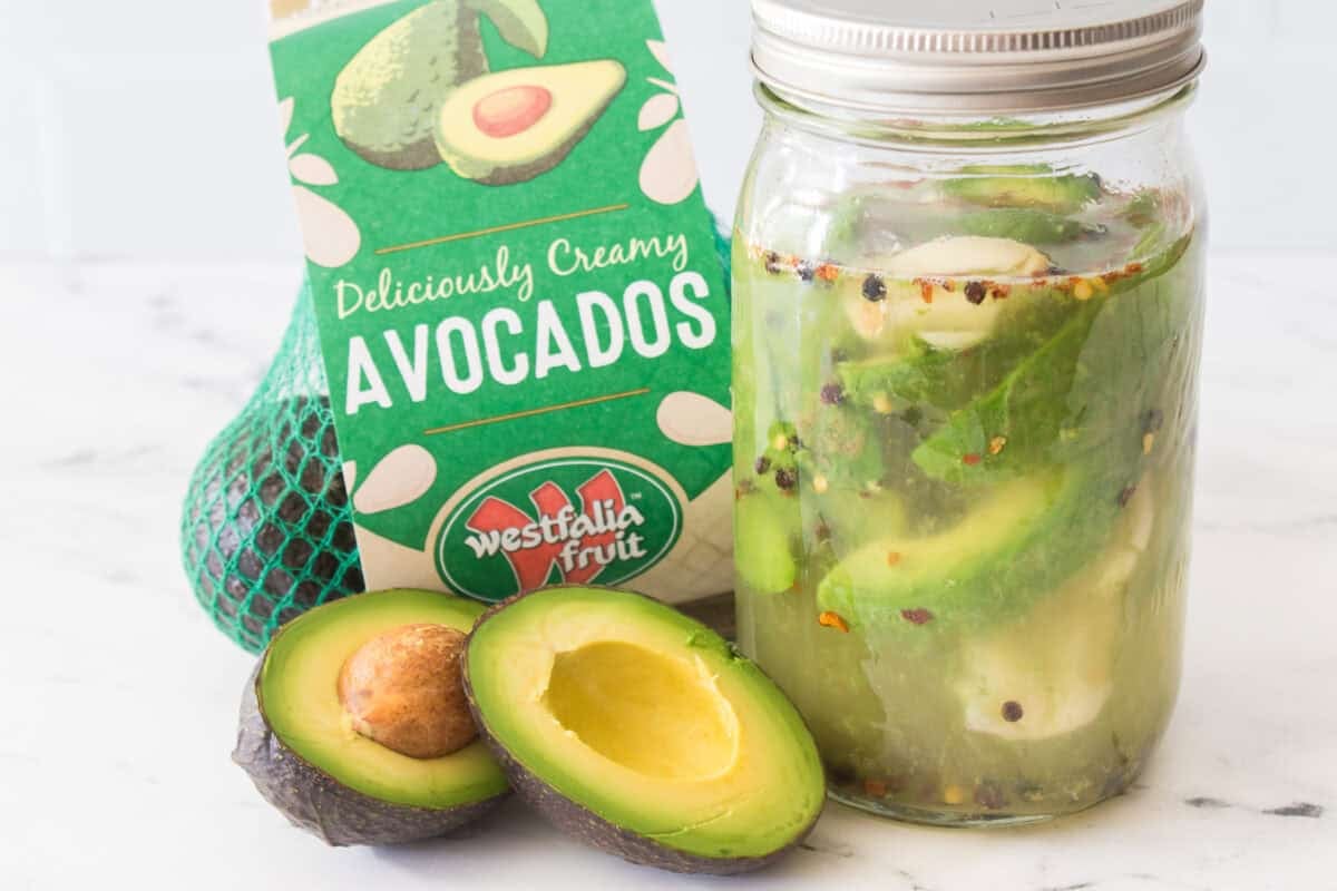 bag of westfalia fruit avocados with avocado cut in half and big mouth mason jar with pickled avocados