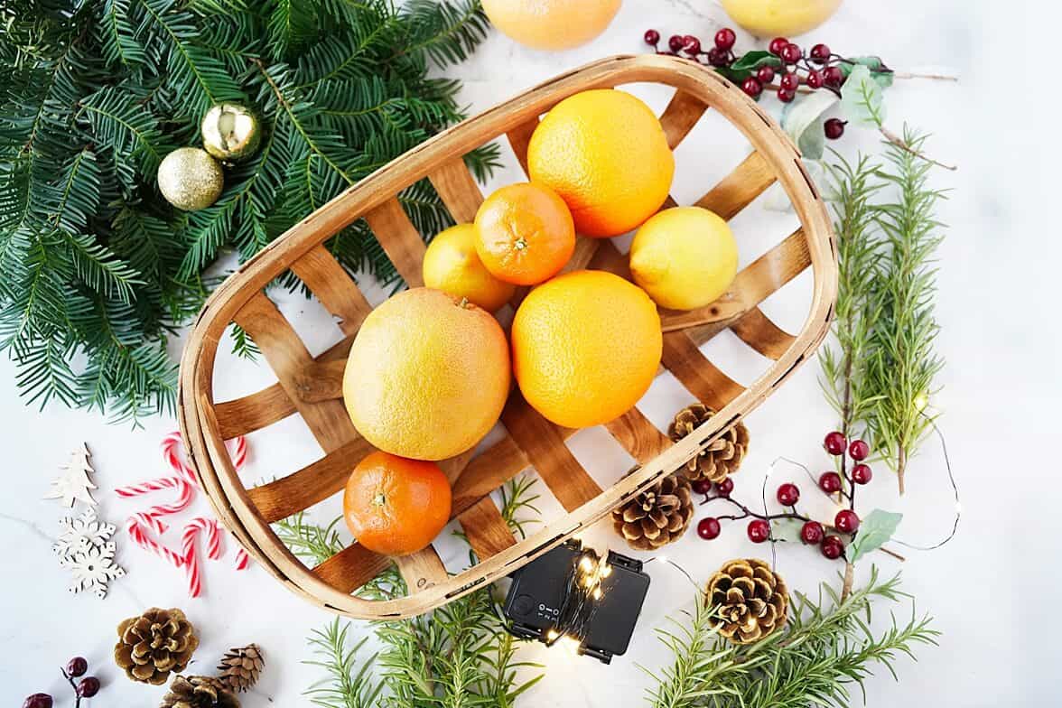 Alll the items needed for Citrus Holiday Centerpiece: citrus, pine cones, pine branches, mini ornaments, twinkle lights, cranberries